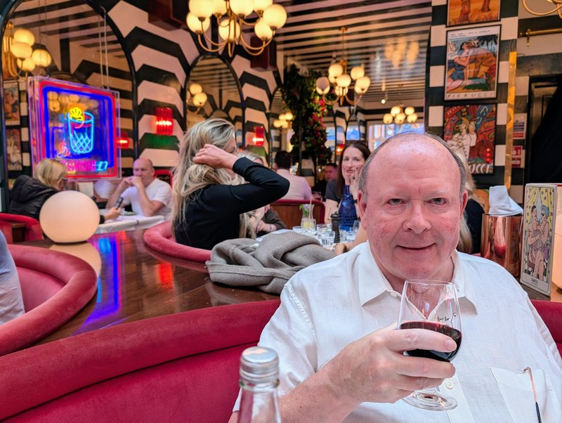 Ken with a glass of wine in a festive restaurant